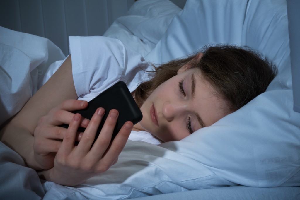 Girl Texting On Mobile Phone At Night While Lying In Bed